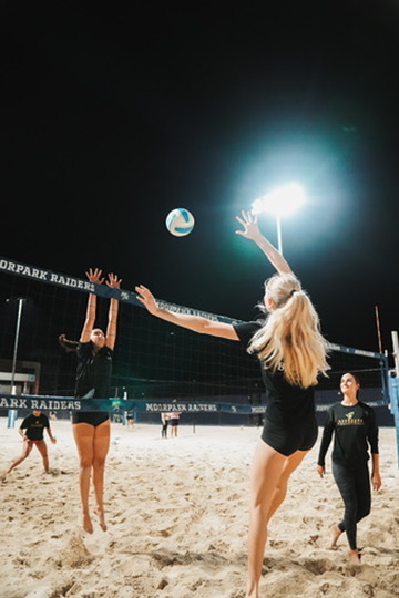 Beach volleyball players battling at the net under stadium lights