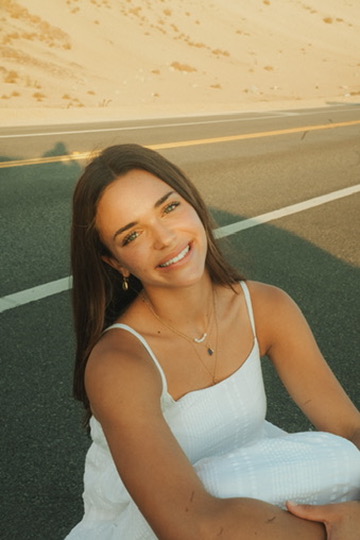 Woman in a white dress smiling on a desert road at golden hour