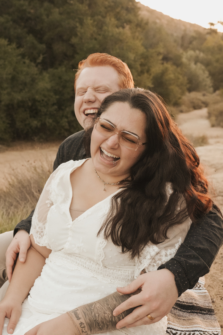 Couple bursting into laughter on a blanket in golden fields