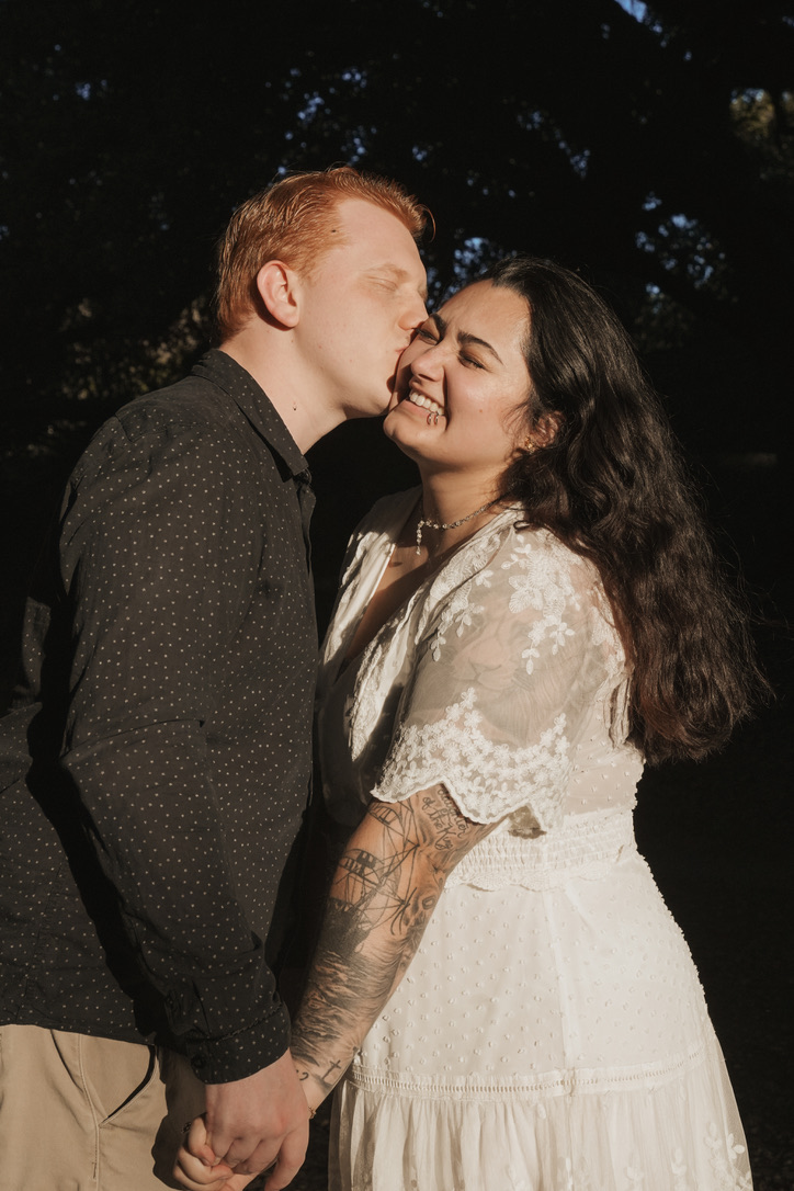 Groom-to-be kissing his fiancee's cheek as she laughs