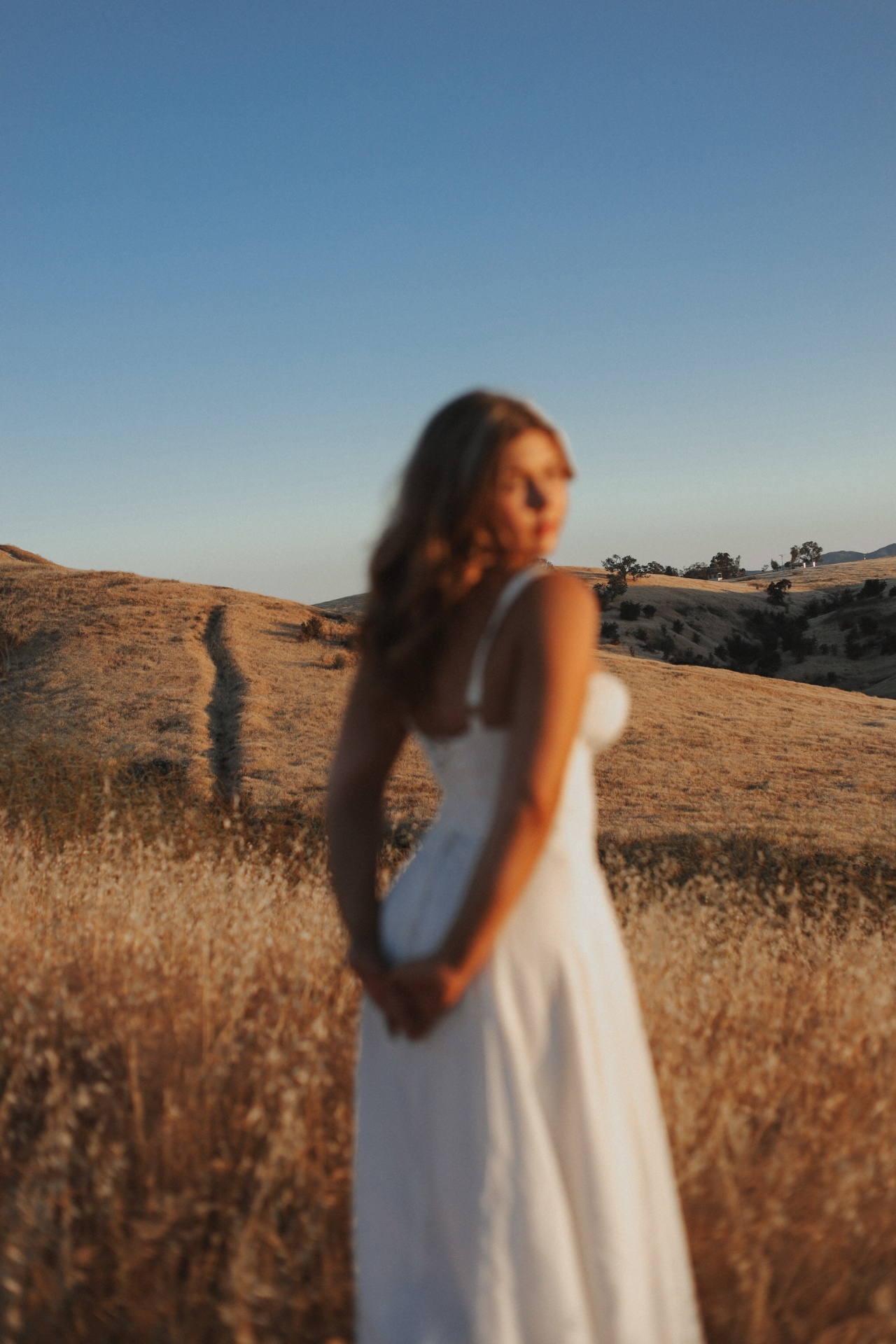 Dreamy soft-focus portrait in a white dress over rolling golden hills