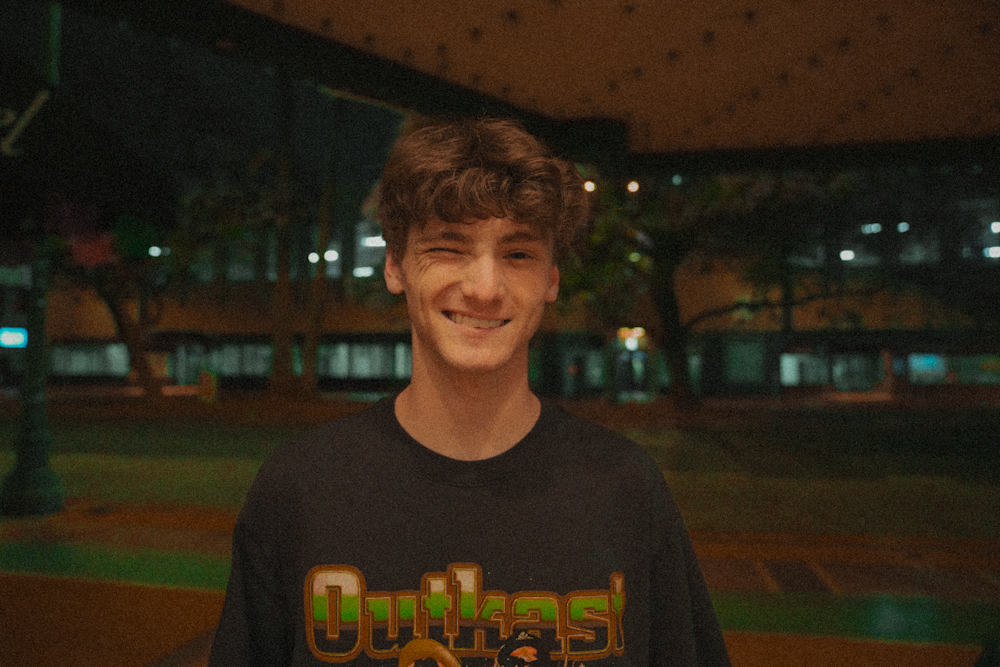 Young man winking and smiling under city lights at night