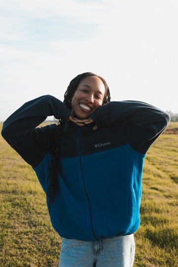 Woman in a blue fleece smiling in a sunlit meadow