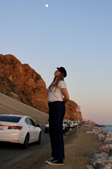 Woman gazing up at the moon along the coastal highway at dusk