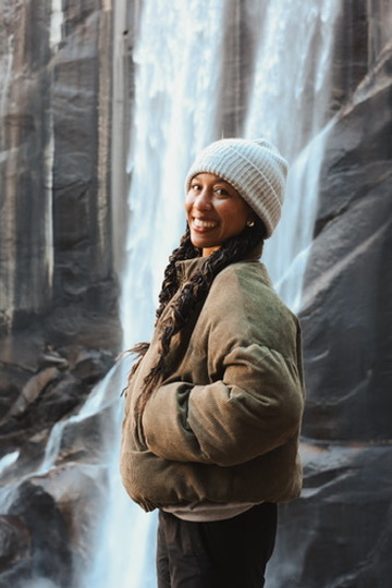 Woman in a beanie smiling in front of a cascading waterfall