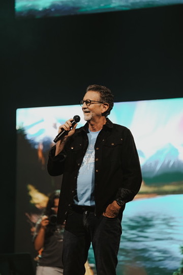 Speaker on stage with a microphone in front of a scenic backdrop