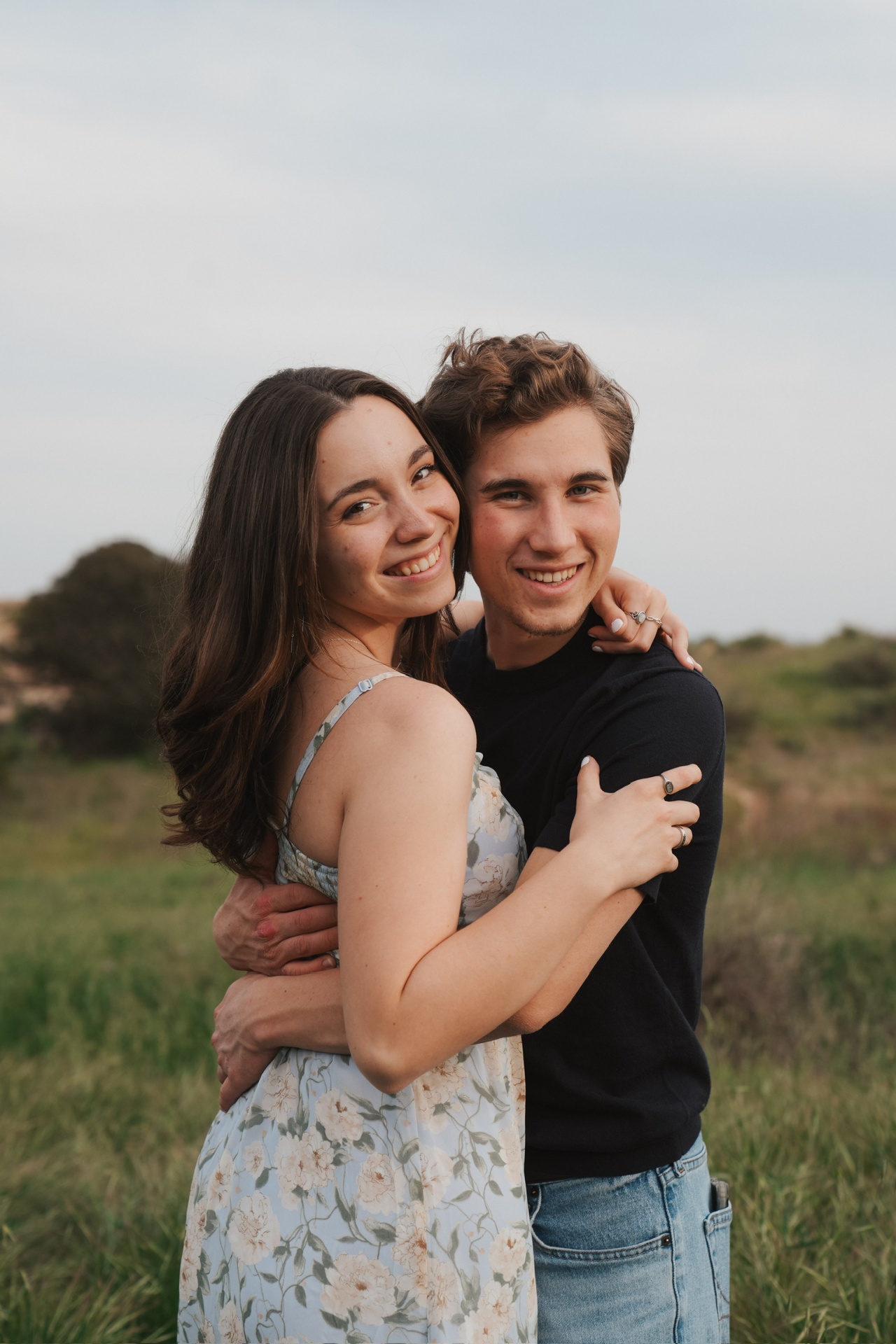 Couple hugging and smiling at the camera in a grassy meadow