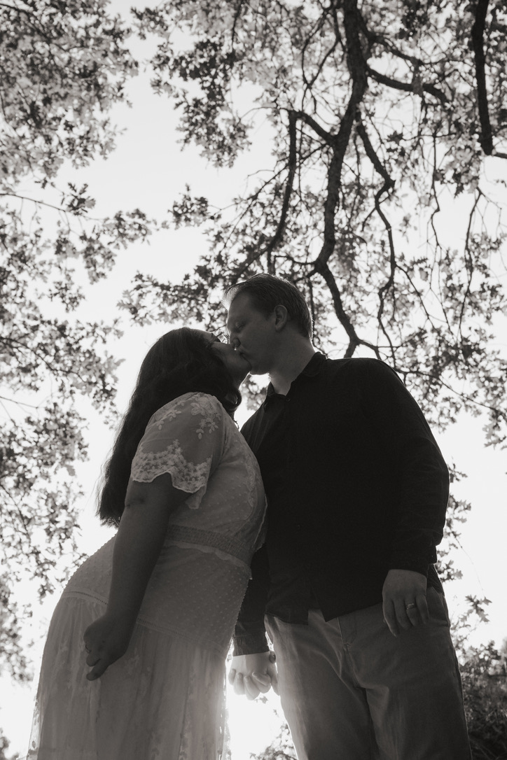 Black and white photo of a couple kissing beneath oak branches