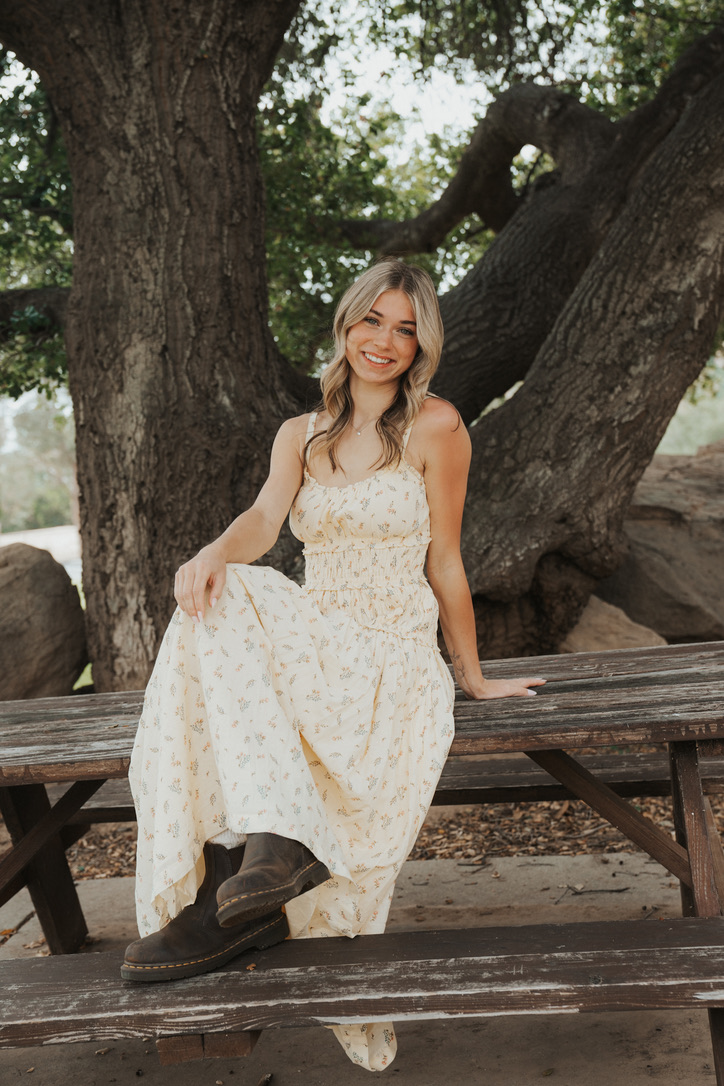 Senior portrait seated on a rustic picnic table beneath an oak