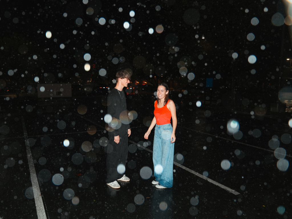 Couple laughing in the rain on an empty lot at night