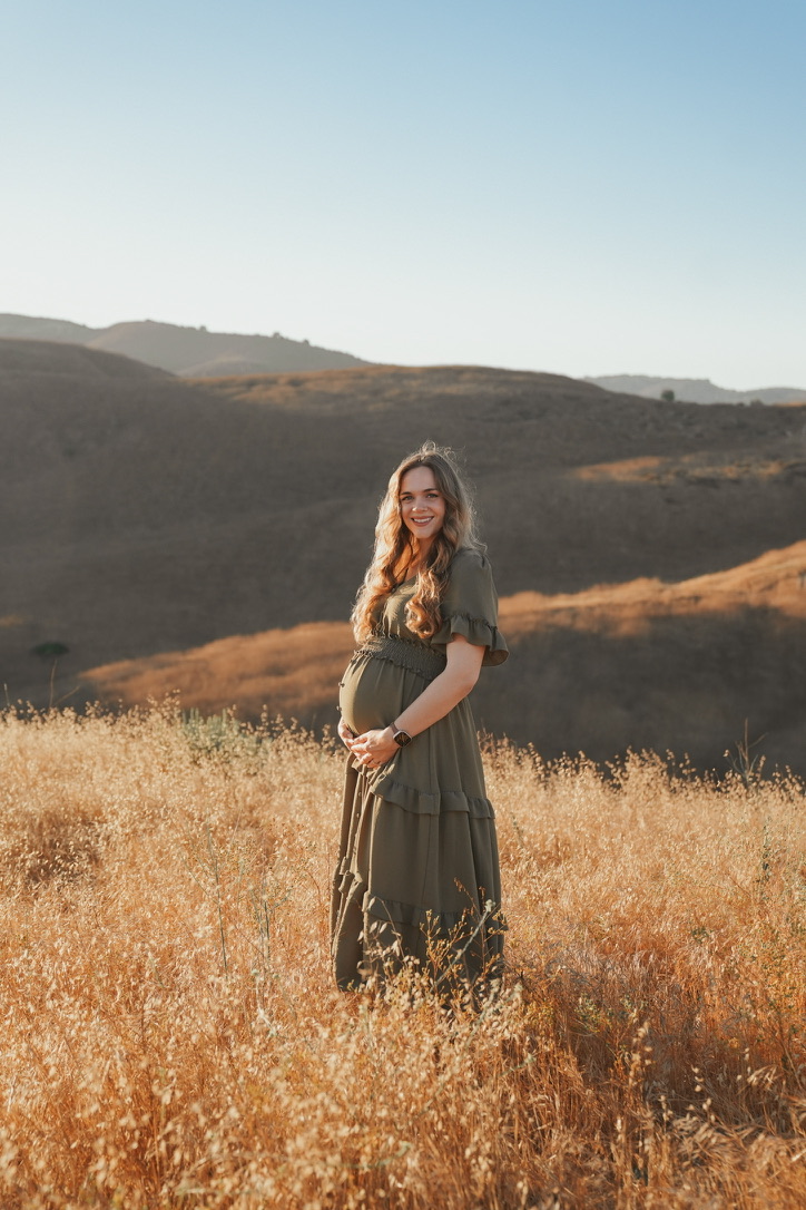 Maternity portrait in an olive dress among golden rolling hills