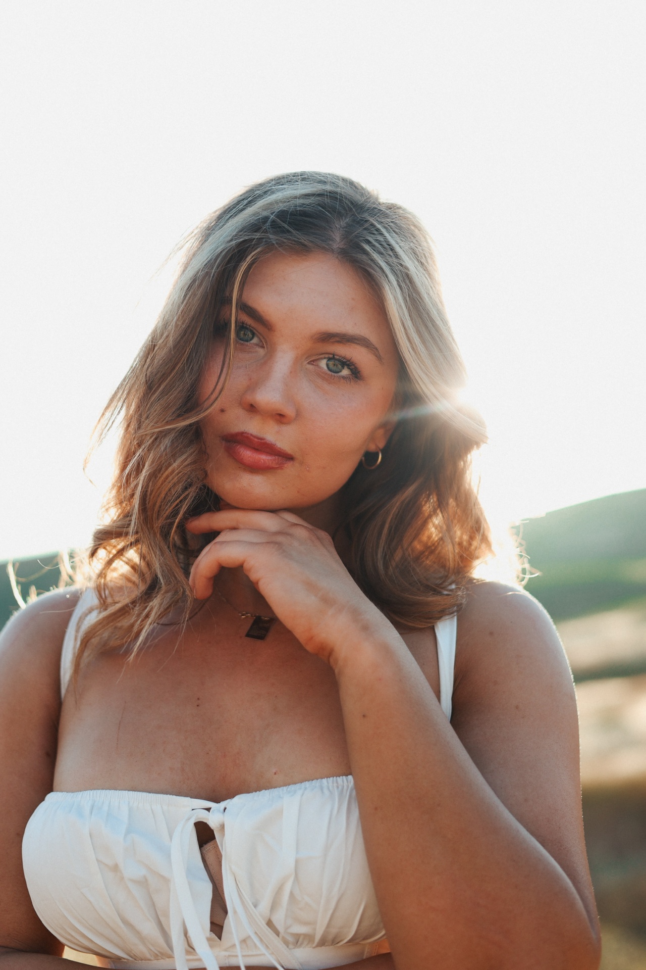 Backlit golden-hour portrait with hand resting under the chin