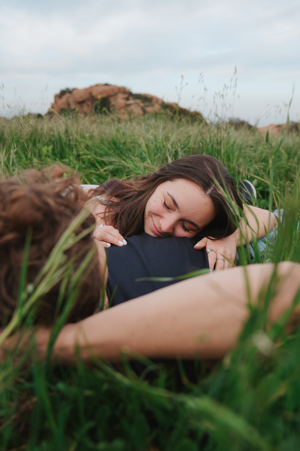 Resting her head on his chest in tall green grass below red rocks