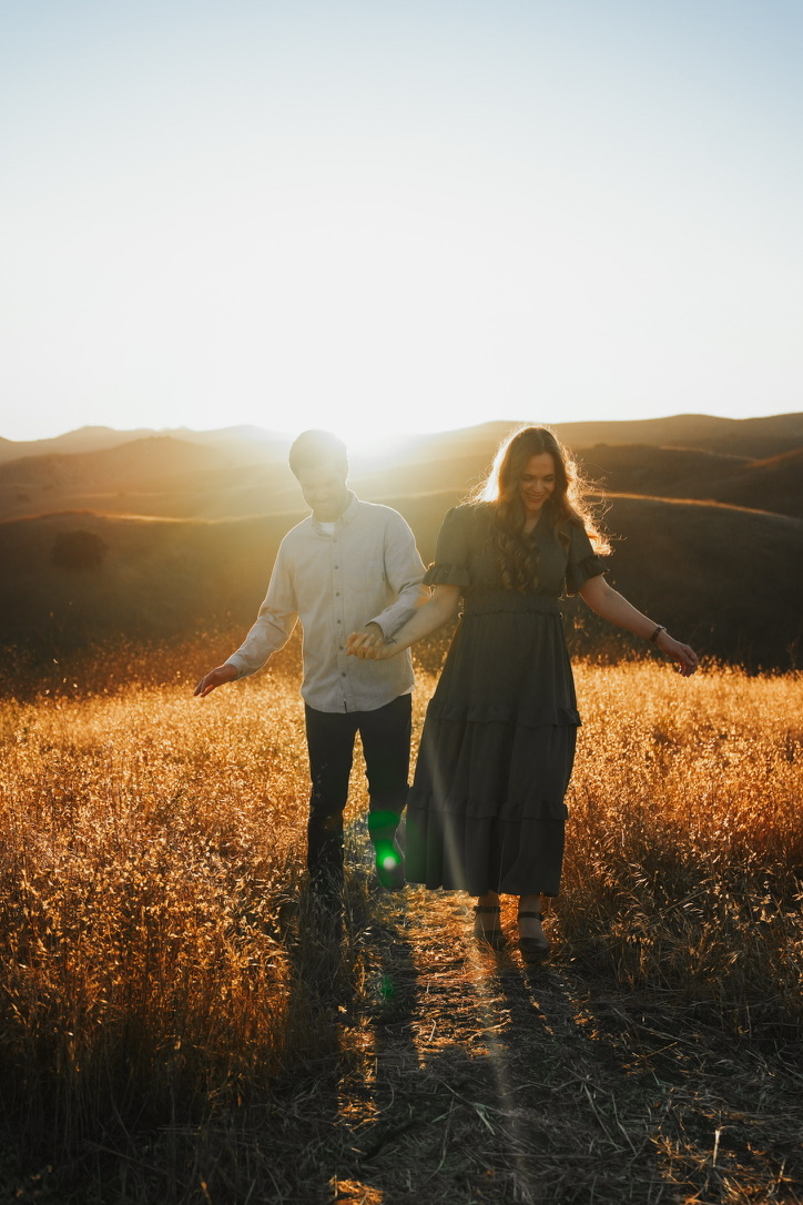Couple walking hand in hand through a golden field at sunset