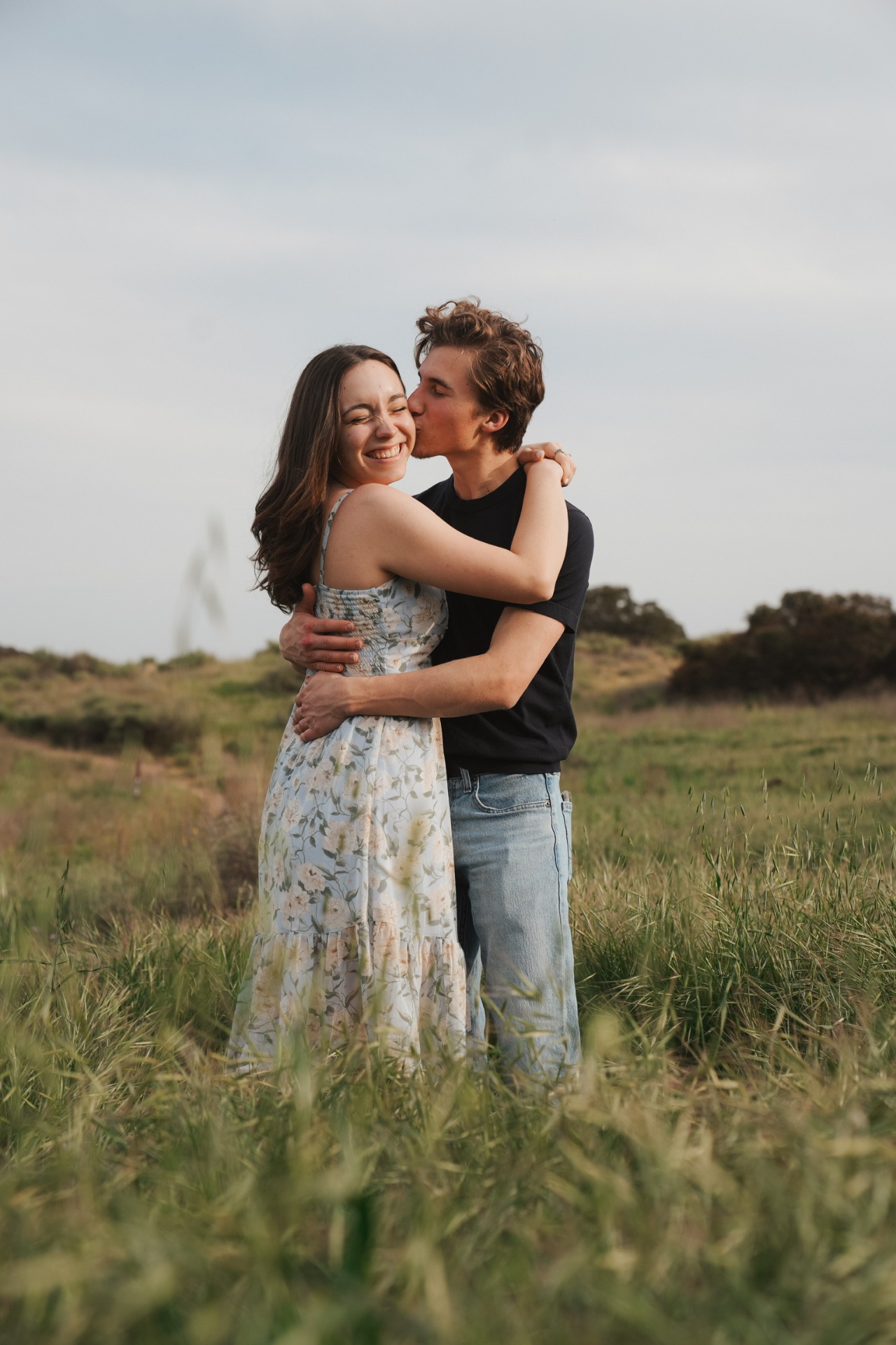 Cheek kiss and a beaming smile in a breezy meadow