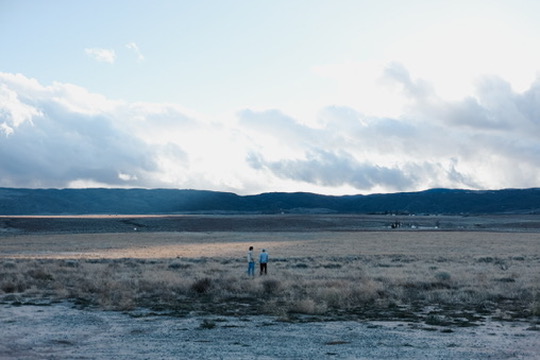 Couple standing small in a vast valley beneath dramatic clouds