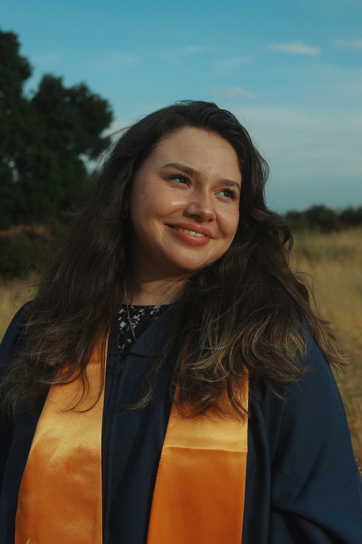 Graduate with an orange stole smiling under a blue sky