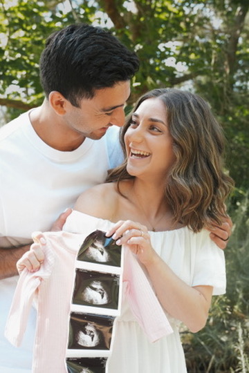 Couple revealing baby ultrasounds pinned to a tiny onesie