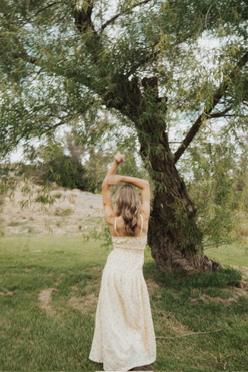 Woman in a floral dress dancing beneath a willow tree