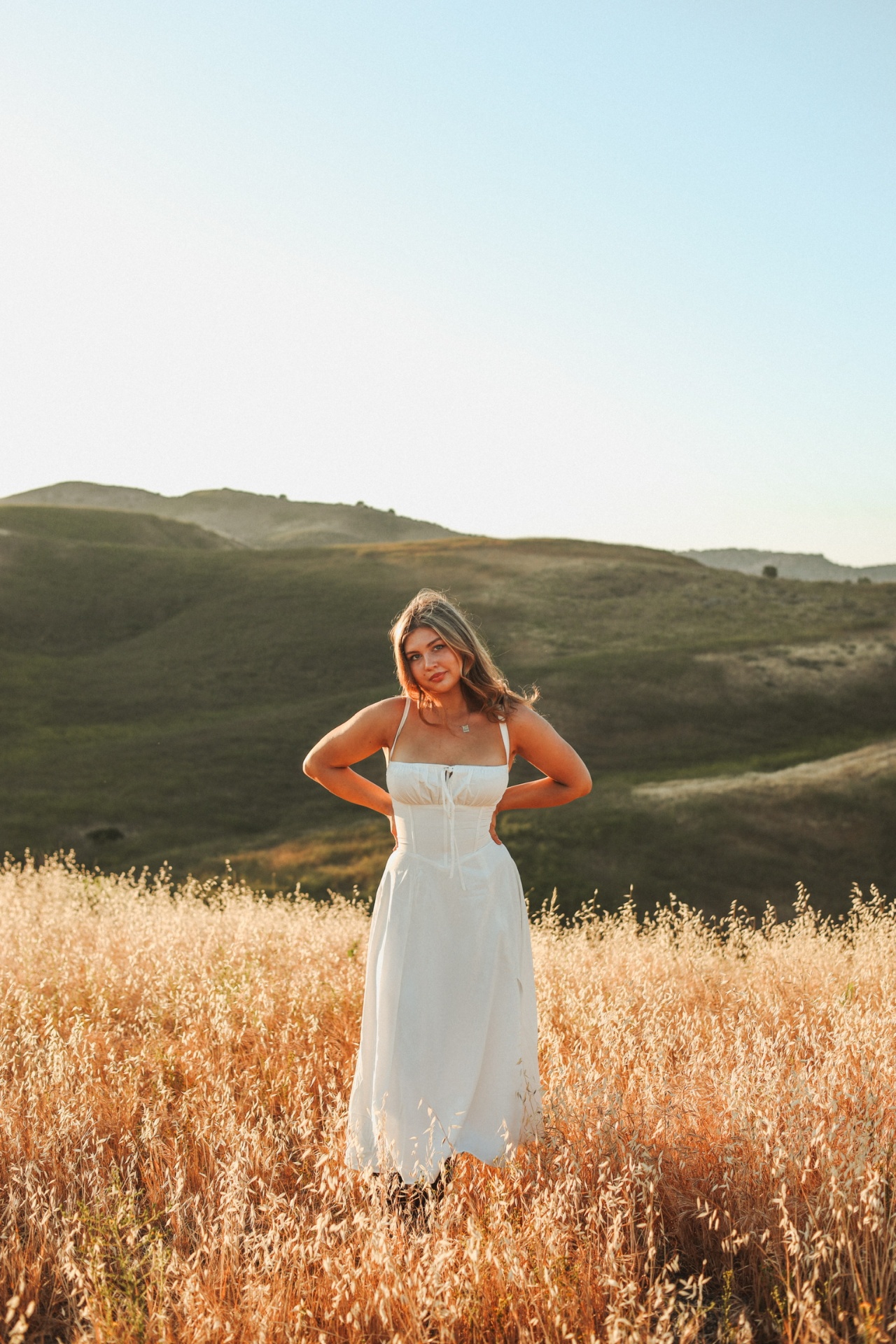 Standing tall in a white dress on a hilltop meadow above green hills