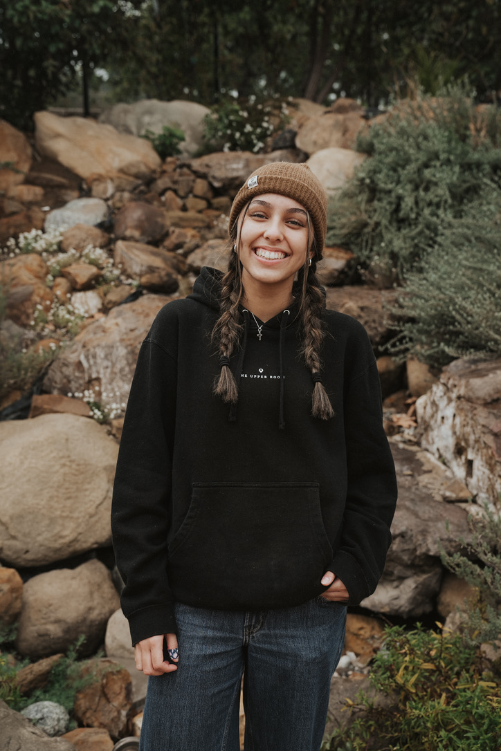 Smiling woman with braids and a beanie by a rocky garden