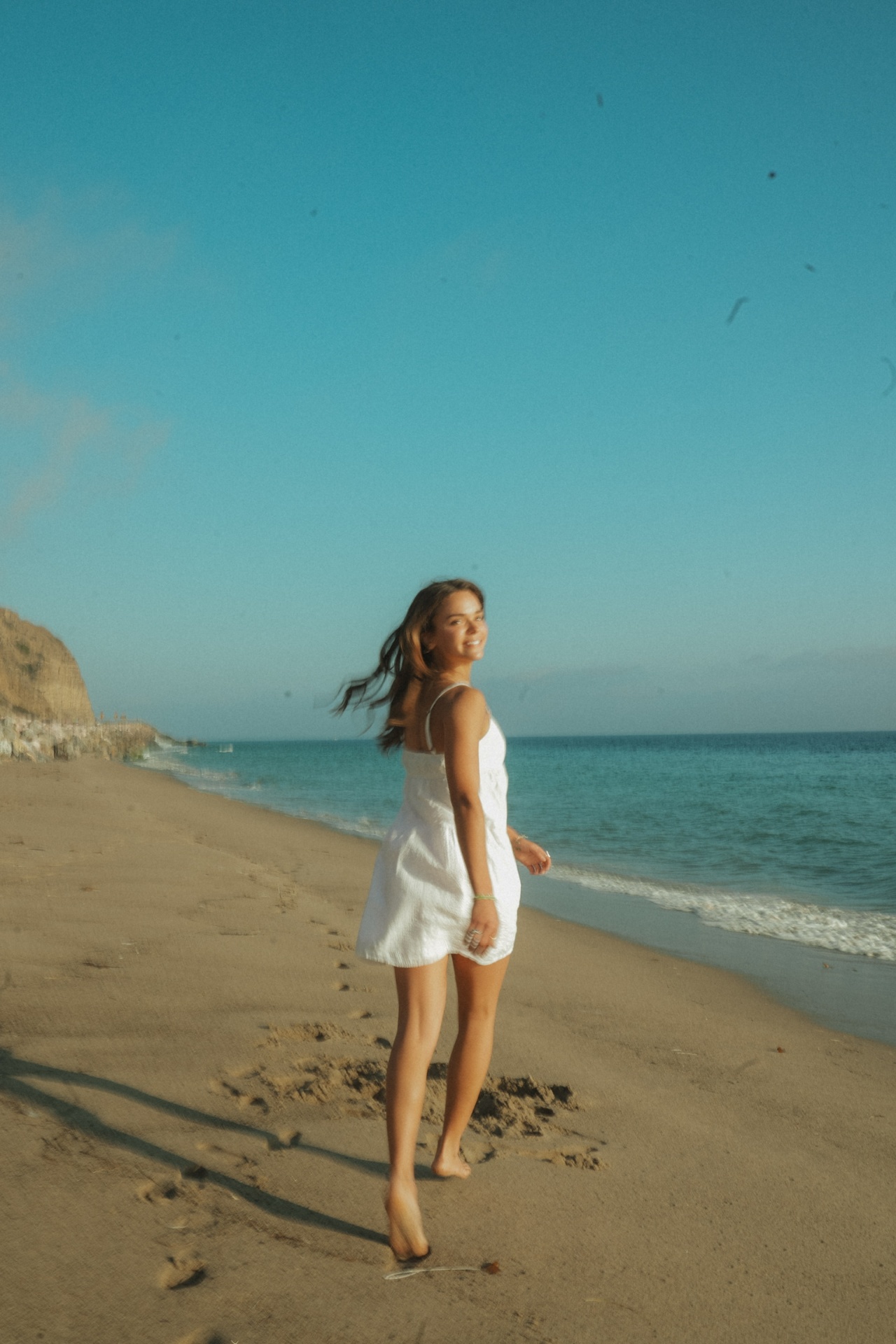 Barefoot look back walking along the shoreline in a white sundress