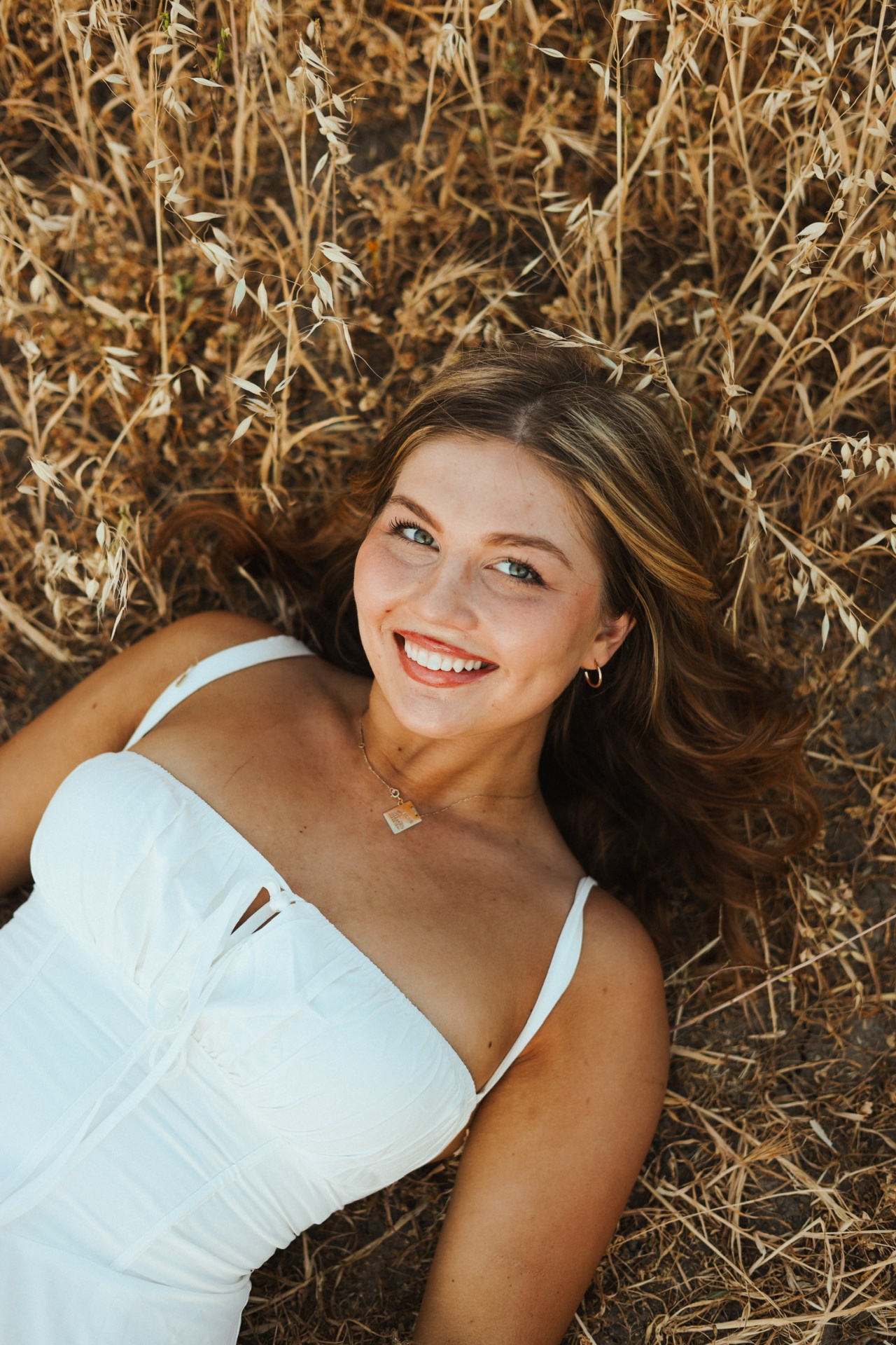 Lying back in golden oats with a bright smile and gold hoops