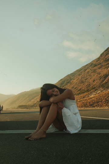 Woman sitting peacefully on a mountain road at sunset