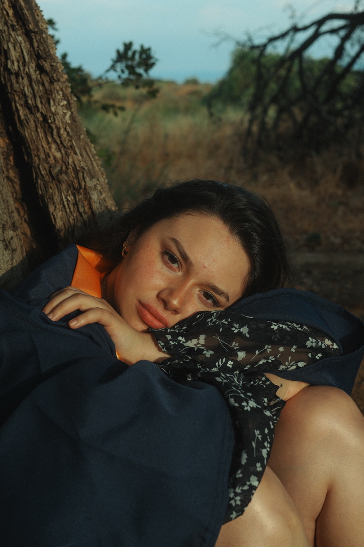 Moody graduation portrait resting against a tree at dusk