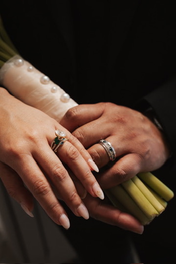 Close-up of newlyweds' hands showing wedding rings over the bouquet