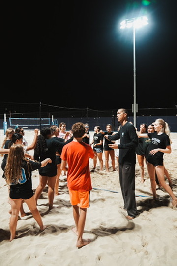 Coach talking to the beach volleyball team huddled on the sand