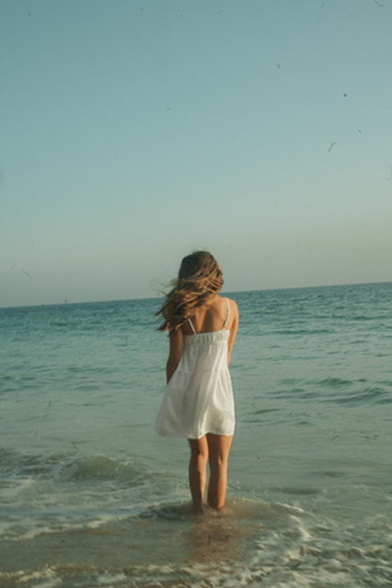 Woman in a white dress wading into the ocean waves