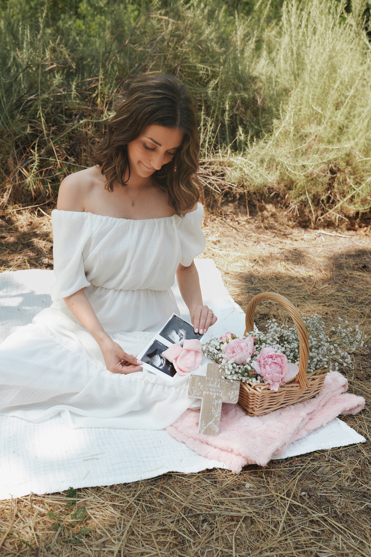 Expecting mother on a picnic blanket with peonies and ultrasound photos