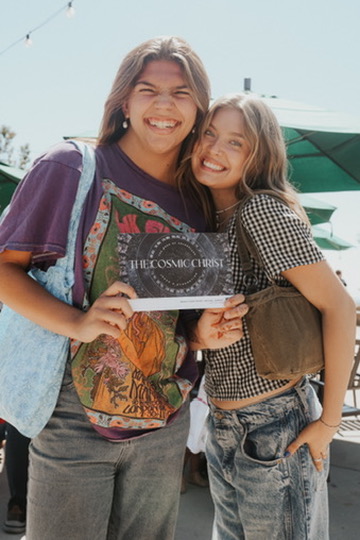 Two friends laughing while holding a book at an outdoor event