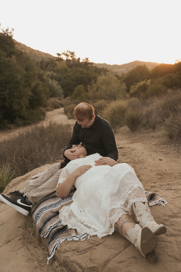 Engaged couple resting on a blanket along a golden canyon trail