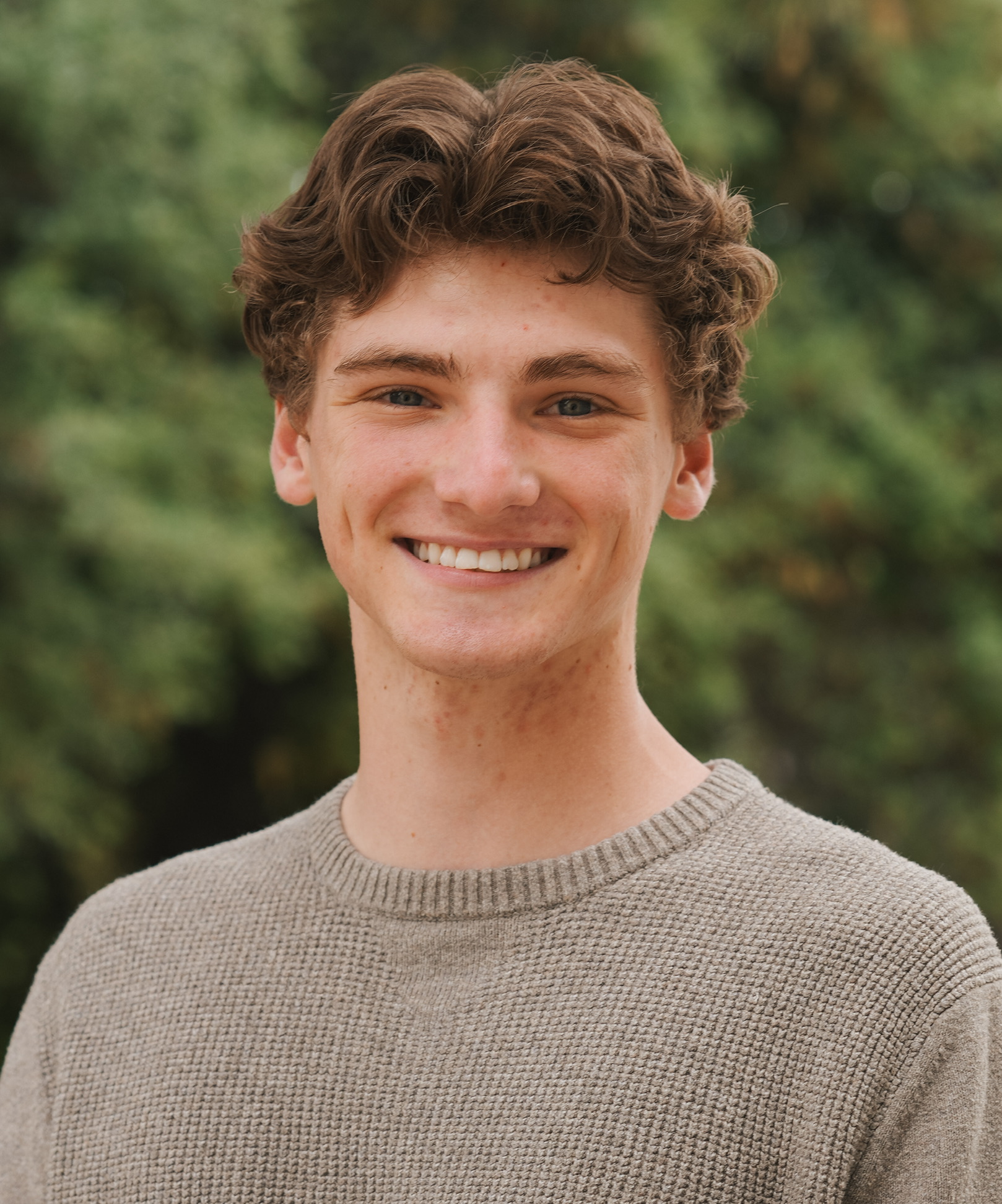 Portrait of a young man smiling in front of greenery