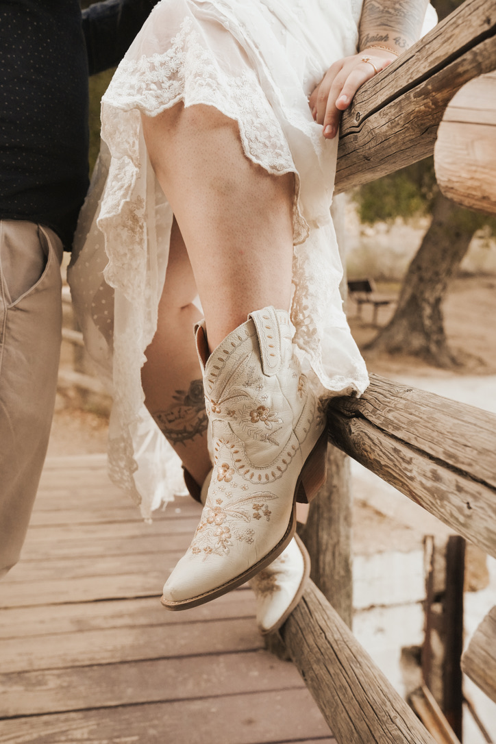 Detail of embroidered cowboy boots and lace dress on a wooden fence